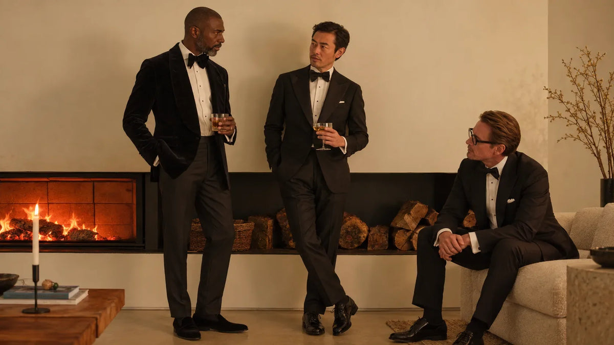 Three men in black-tie tuxedos seated by a fireplace
