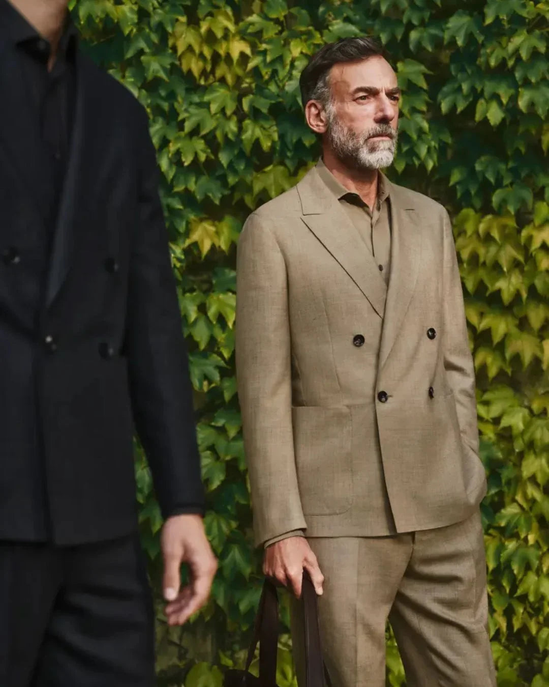 Two men in Zegna tailoring, one in a black suit and one in a double-breasted olive suit