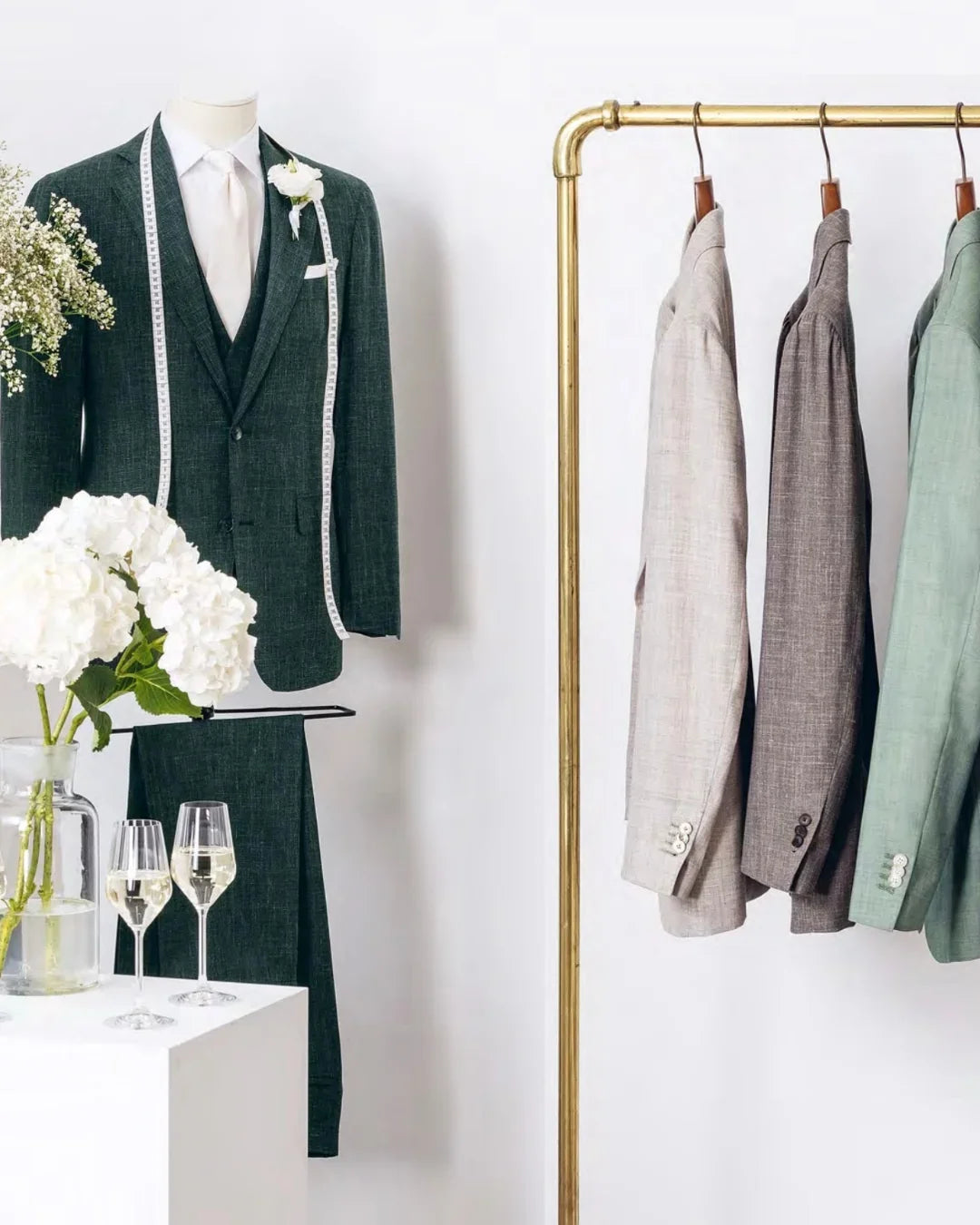 Green wedding suit with white flowers beside a jacket rail