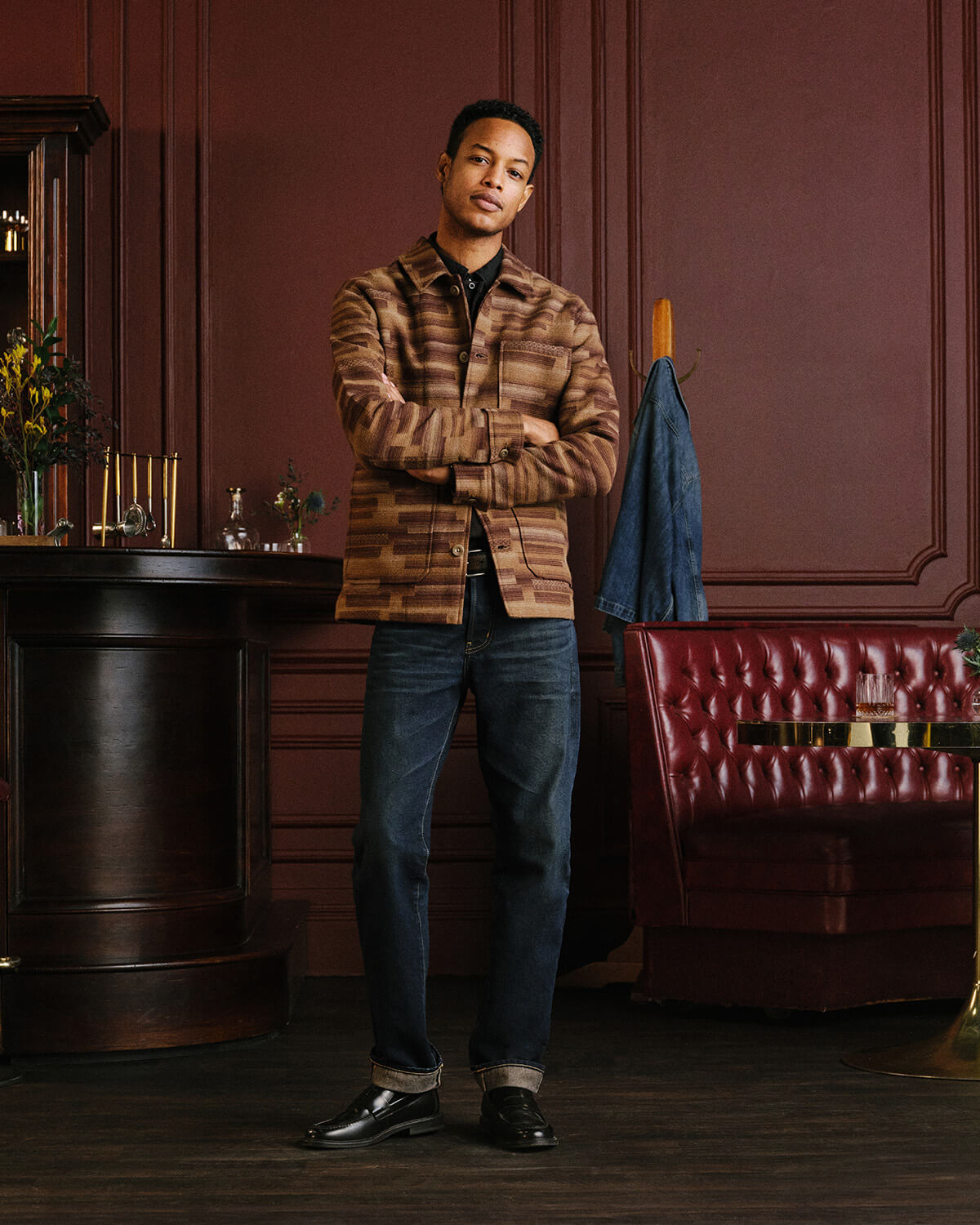Man in a striped shirt and dark AG jeans in a wood-paneled room