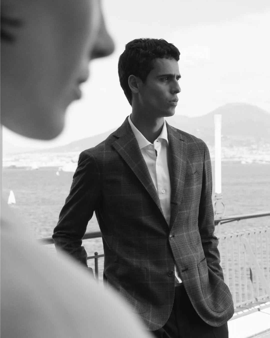 Man in a grey check Barba Napoli jacket and white shirt overlooking the Bay of Naples.