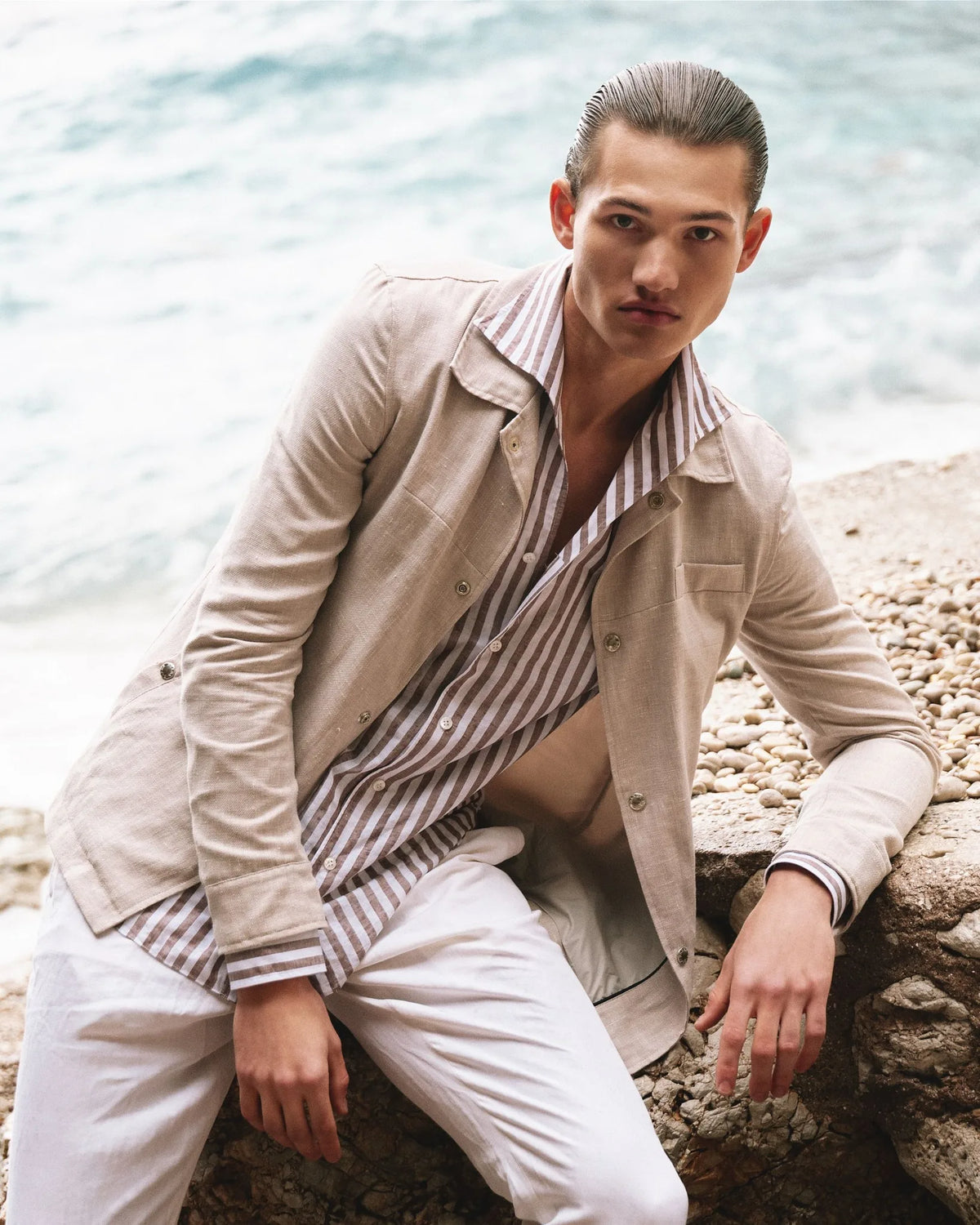 Man in a beige Barba Napoli overshirt and striped shirt by the sea.