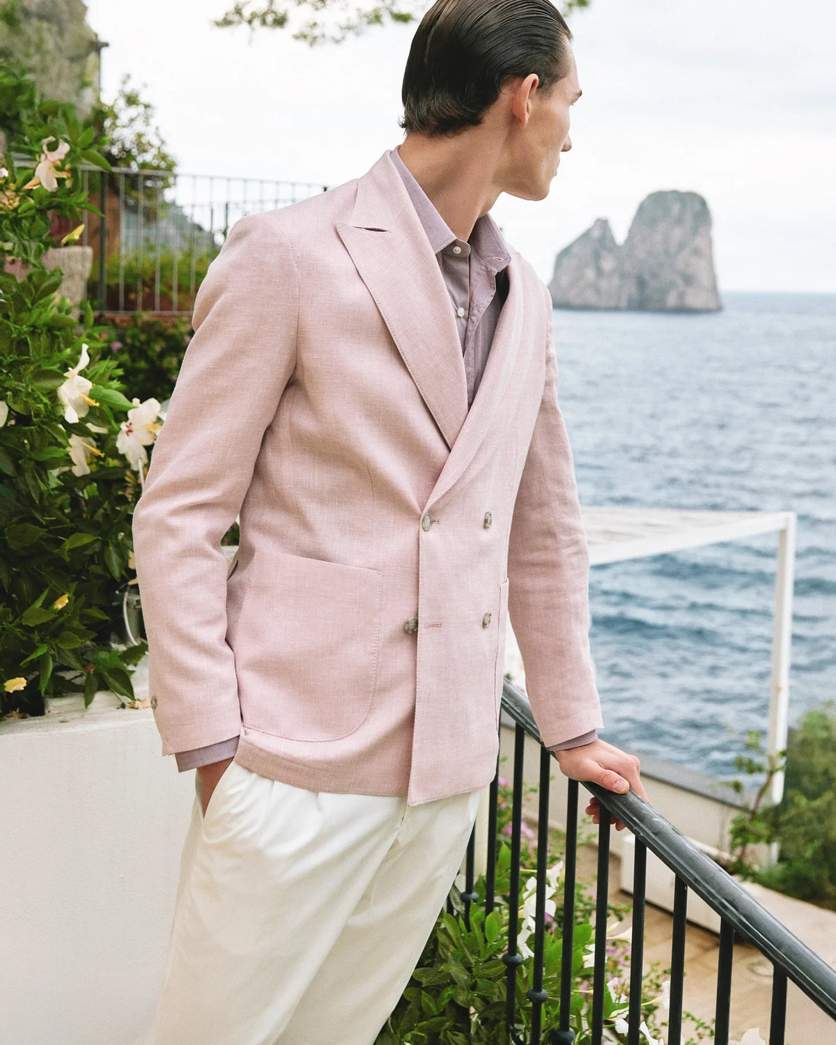 Man in a pink Barba Napoli double-breasted jacket on a terrace facing the Capri Faraglioni.