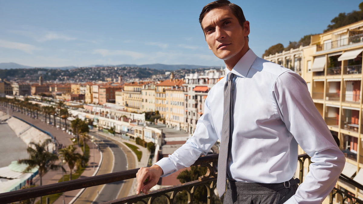 Man in Eton white shirt and gray tie on a seaside balcony