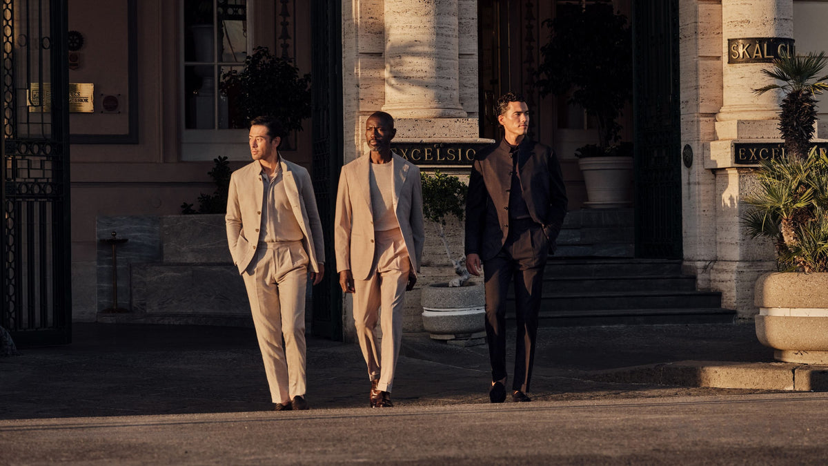 Men in light and dark suits outside a grand hotel at dusk