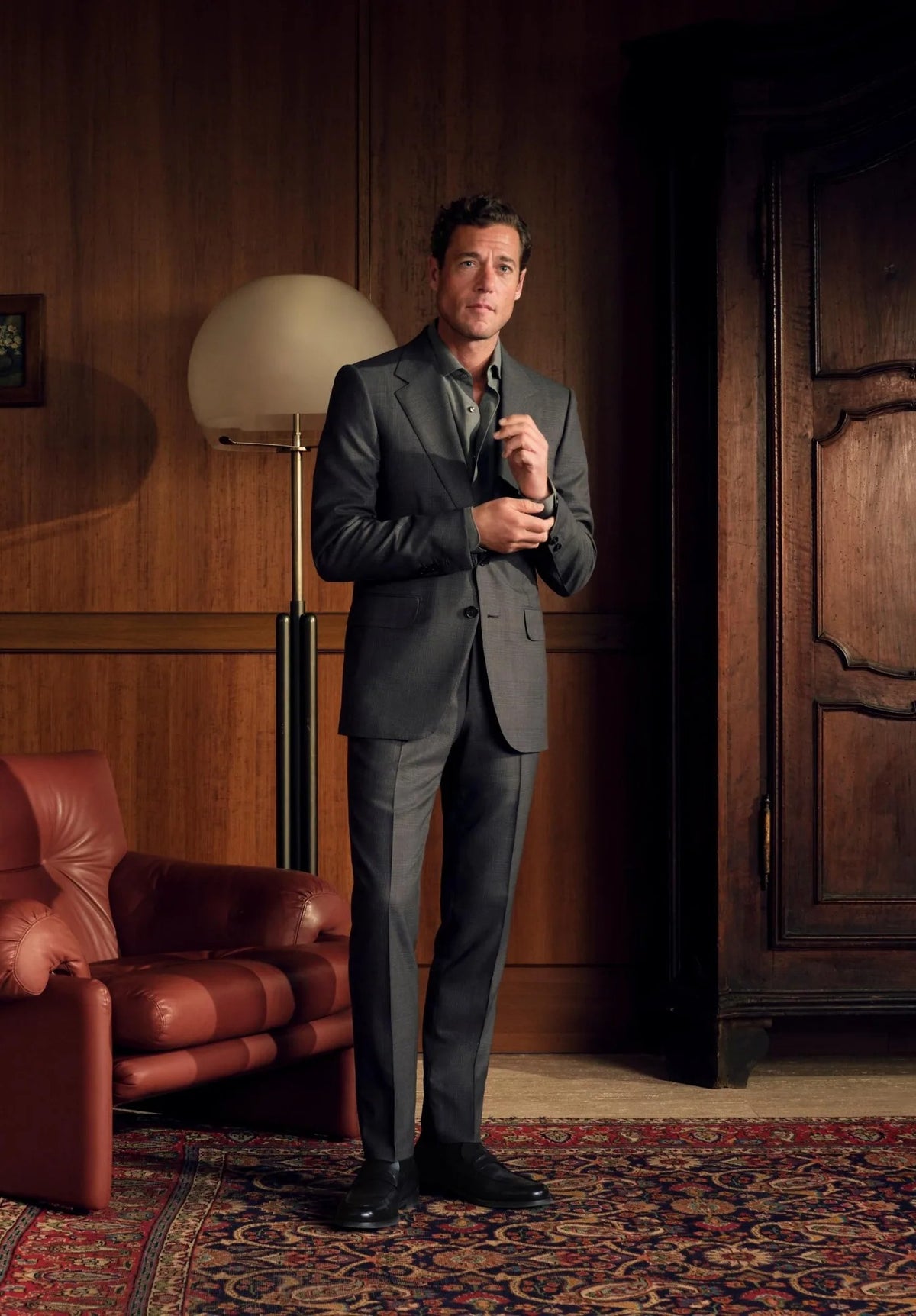 Man in charcoal suit in a wood-paneled study