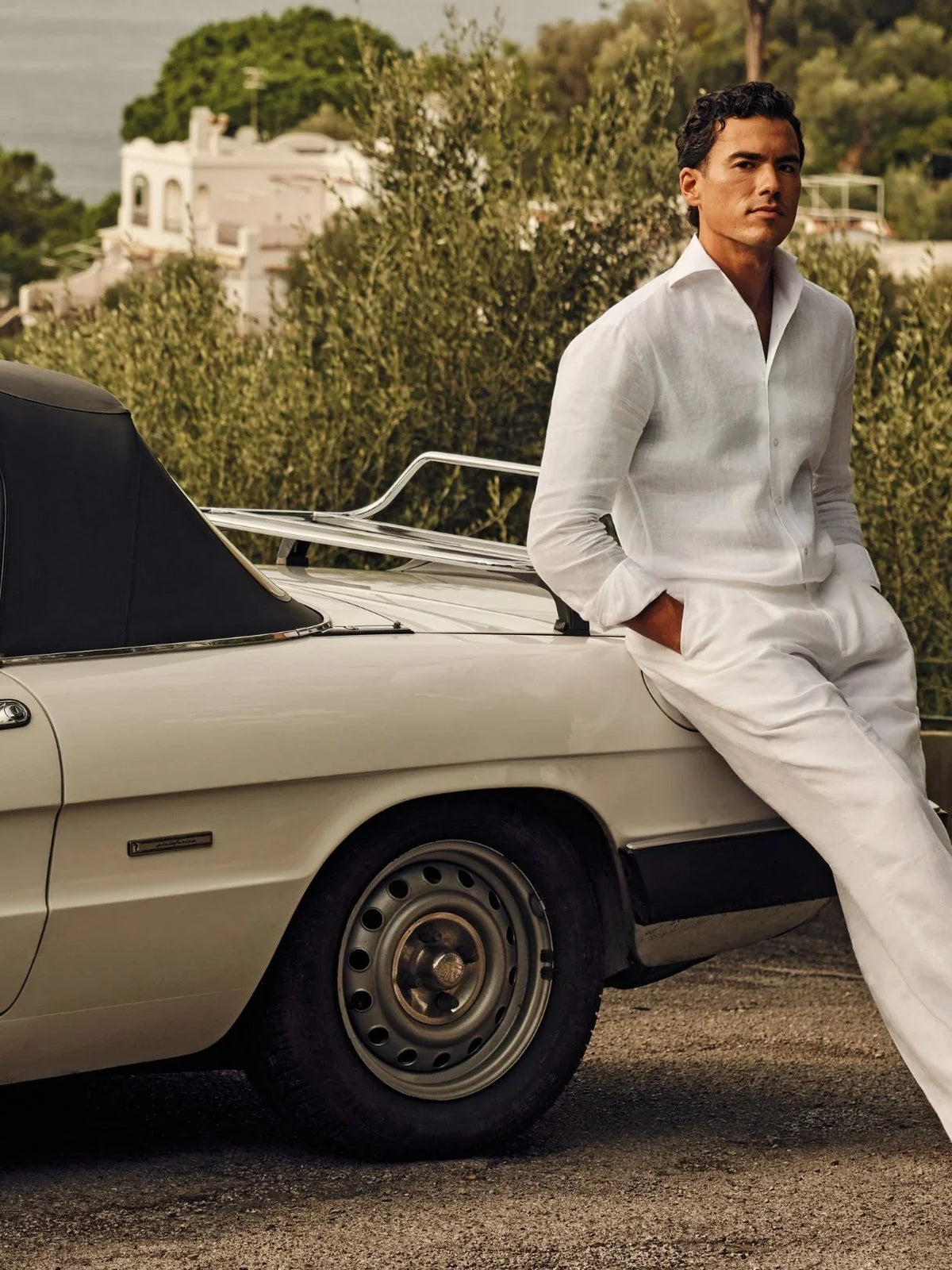 Man in white linen outfit leaning on a vintage convertible