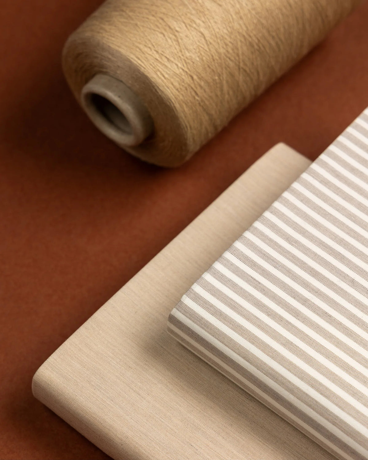 Spool of cotton thread on folded beige and striped Thomas Mason shirting.